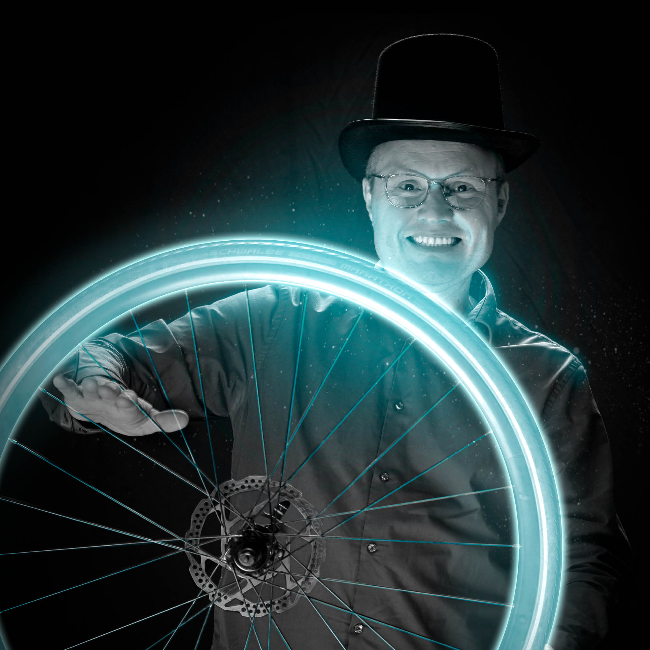 Man met hoed achter verlicht fietswiel lachend