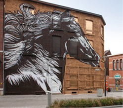 Grote muurschildering van een paard op straatgebouw.