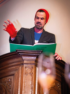 Man leest voor uit groen boek op podium.