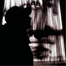 Silhouet van persoon bij raam met gordijnen.