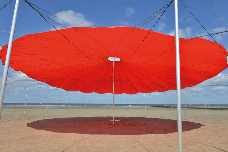 Grote rode zonneparasol op zandstrand, zonnige dag.